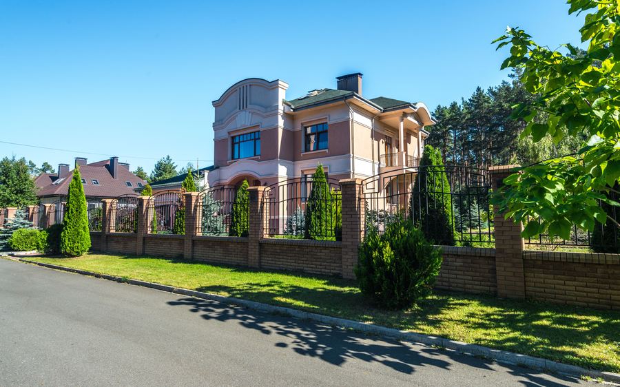 Dark metal fence panels set between brick pillars along the frontage of a large home