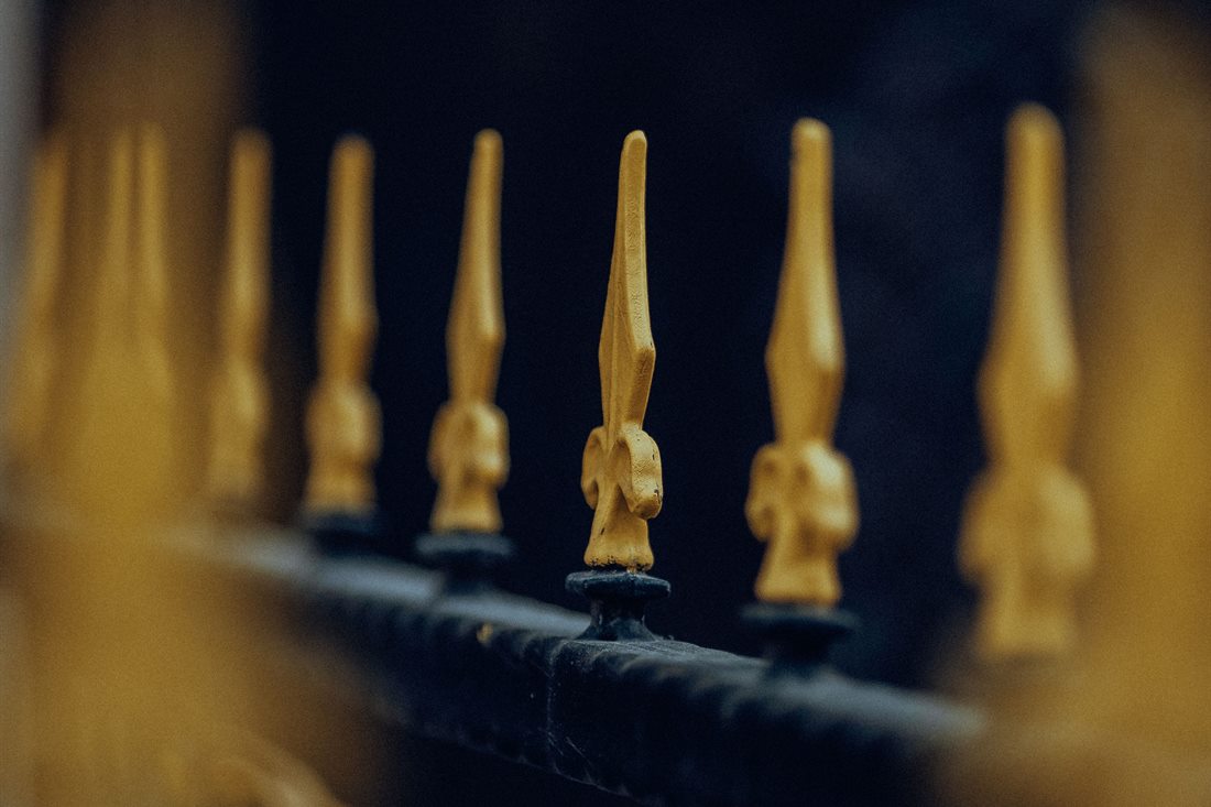 Close-up of gold-painted spear finials along the black top rail of a wrought iron fence