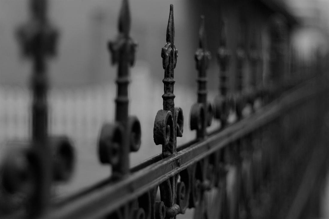 Close-up of a run of ornamental iron fence finials with scrolled collars, in black and white