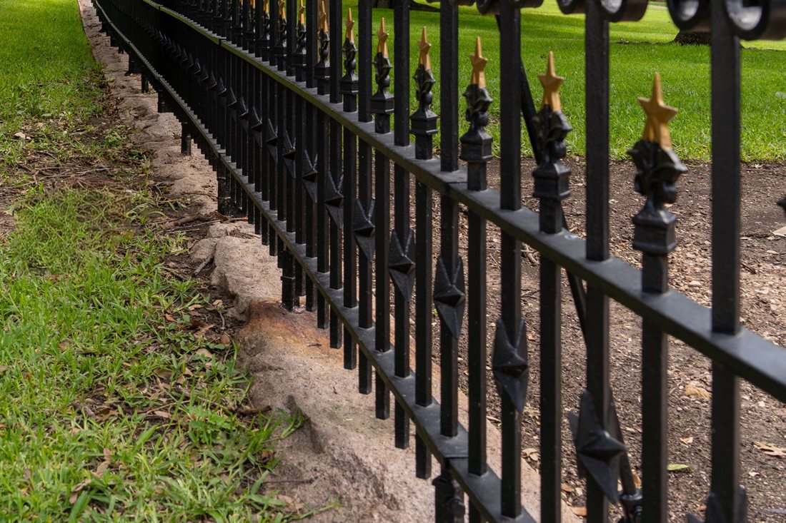 Close-up of a black wrought iron fence with gold star finials running along a grass edge