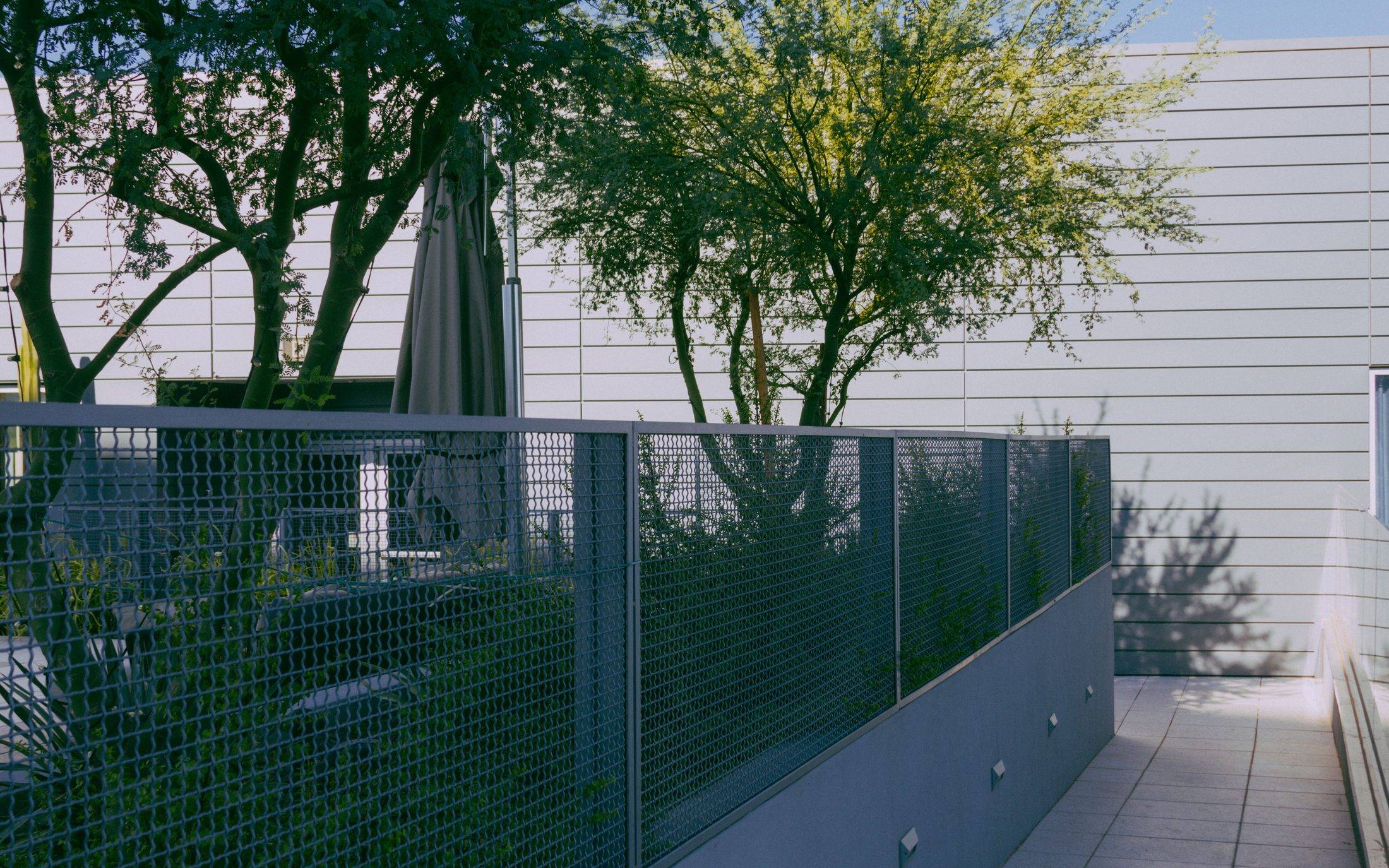 Grey framed metal fence panels on a low wall around a planted patio beside a modern clad building