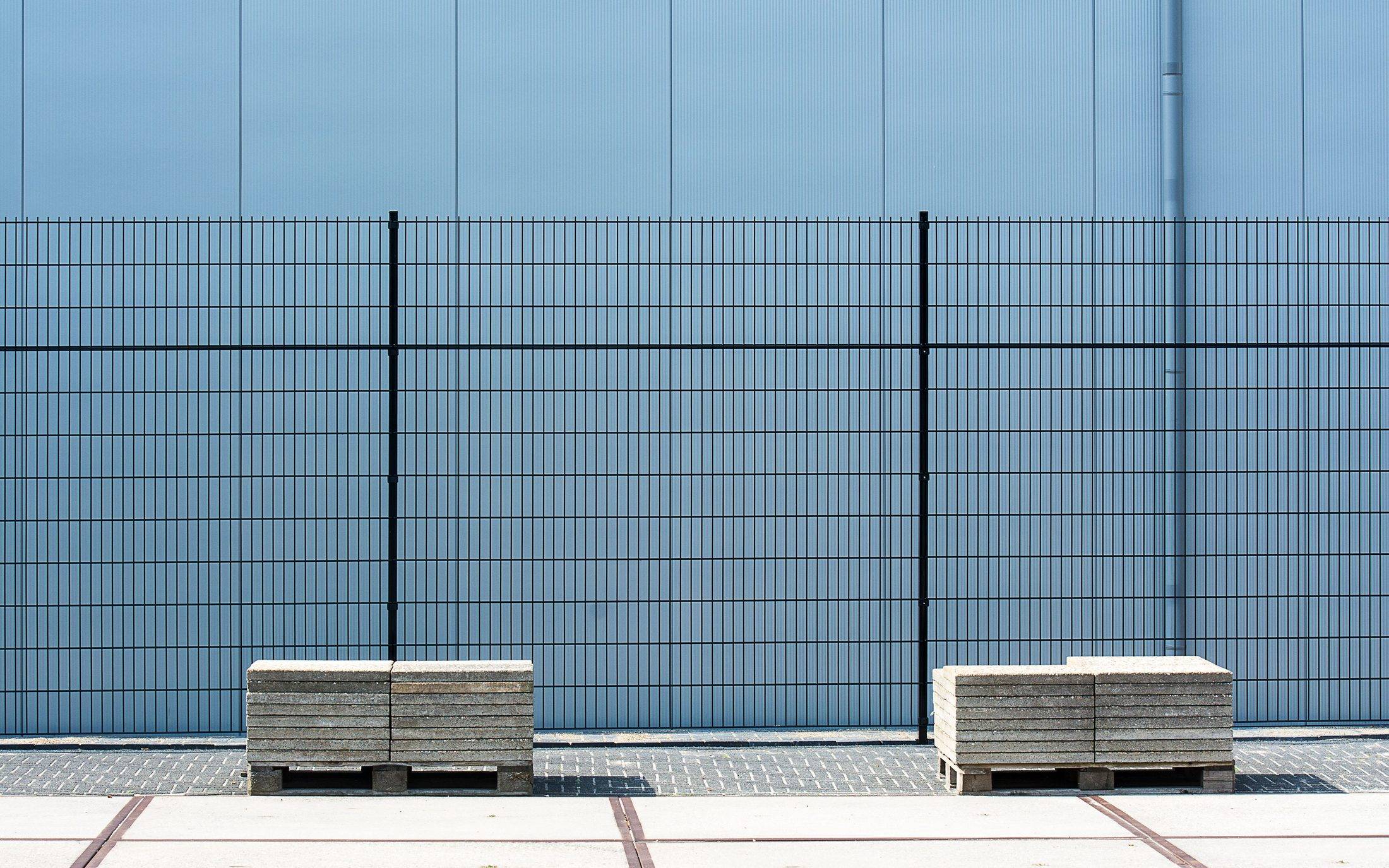 Black welded panel fence running in front of a pale blue industrial building