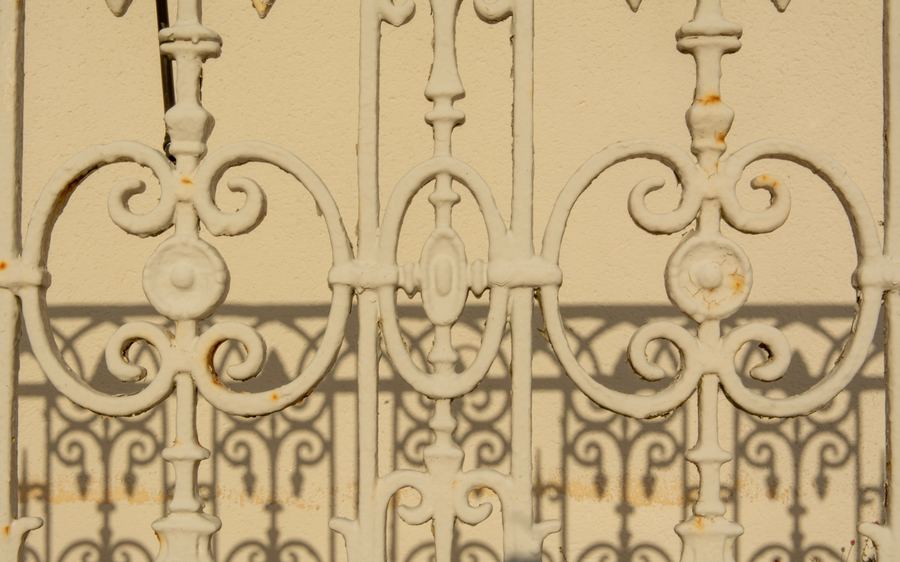 Ornate wrought iron panel with scrolled centre motif set against a rendered wall