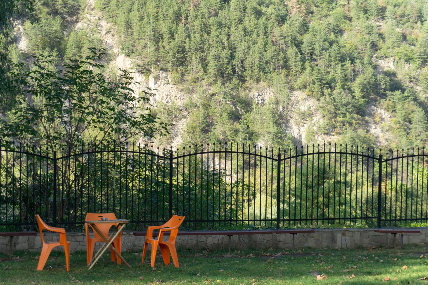 Long run of black arched-top metal picket fence panels along a lawn with orange garden chairs