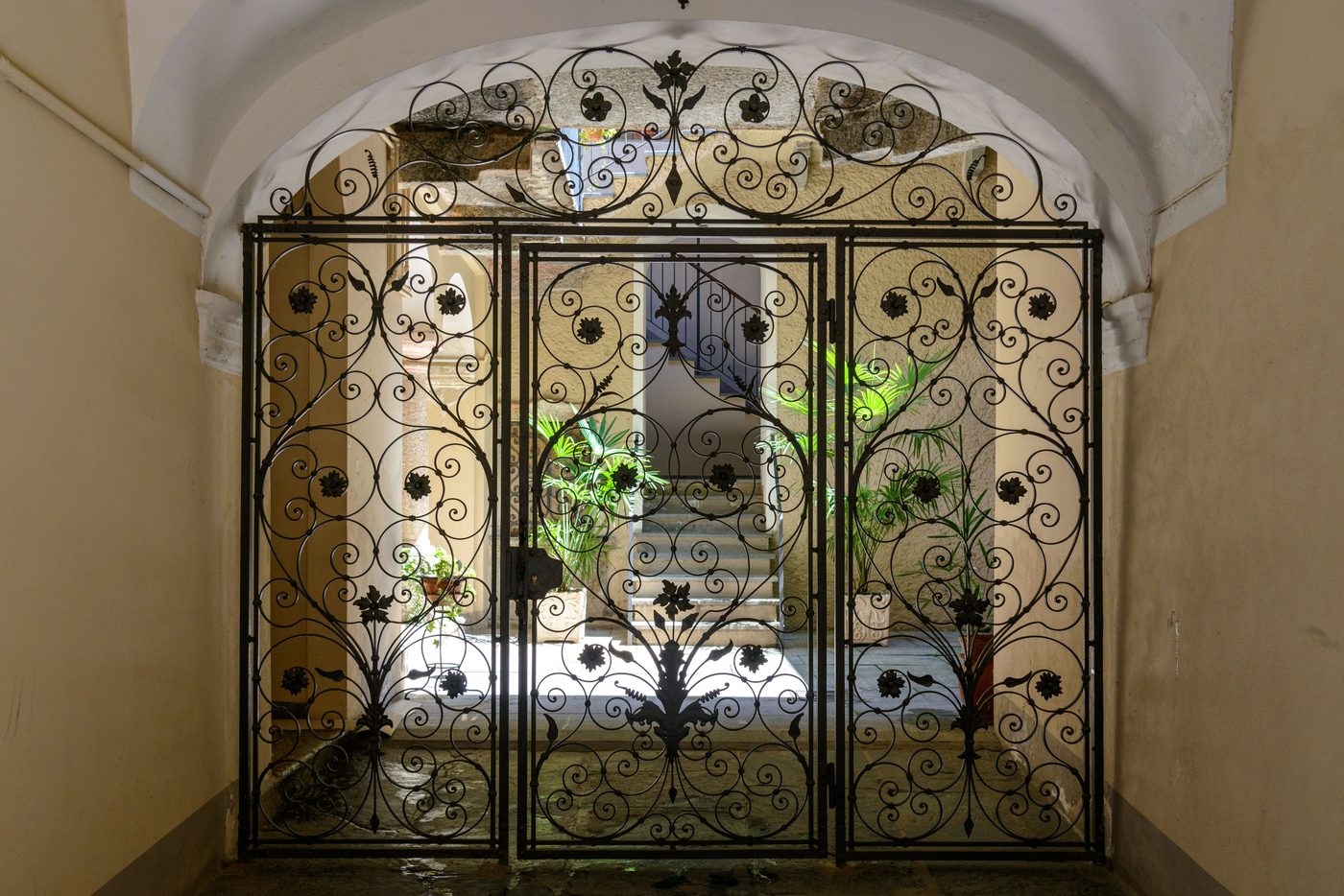 Black ornate wrought iron gate with scrollwork set in a sunlit stone archway