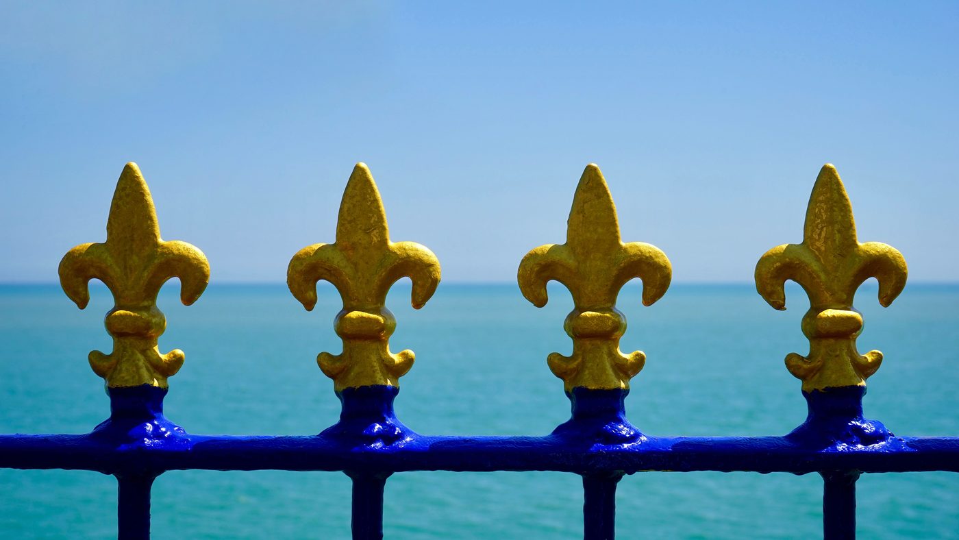 Grey painted wrought iron fence with fleur-de-lis finials in front of a limestone wall