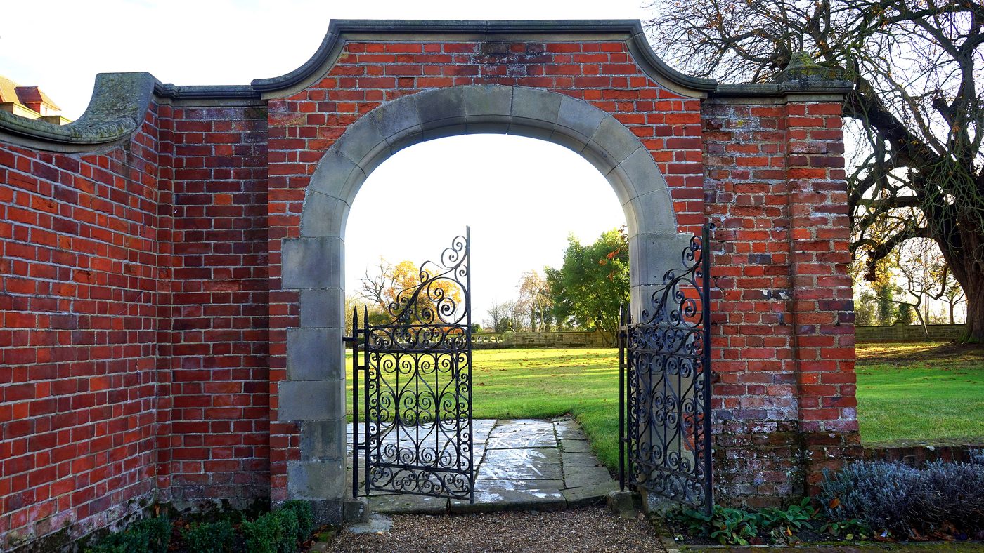 Brick arch with open wrought iron gates leading into a green garden