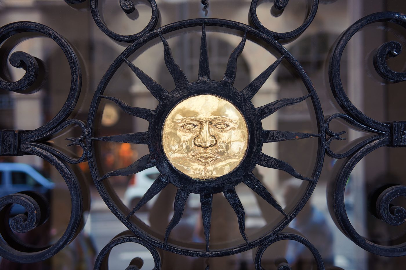 Wrought iron gate scrollwork around a sun ornament with a gold face at its centre
