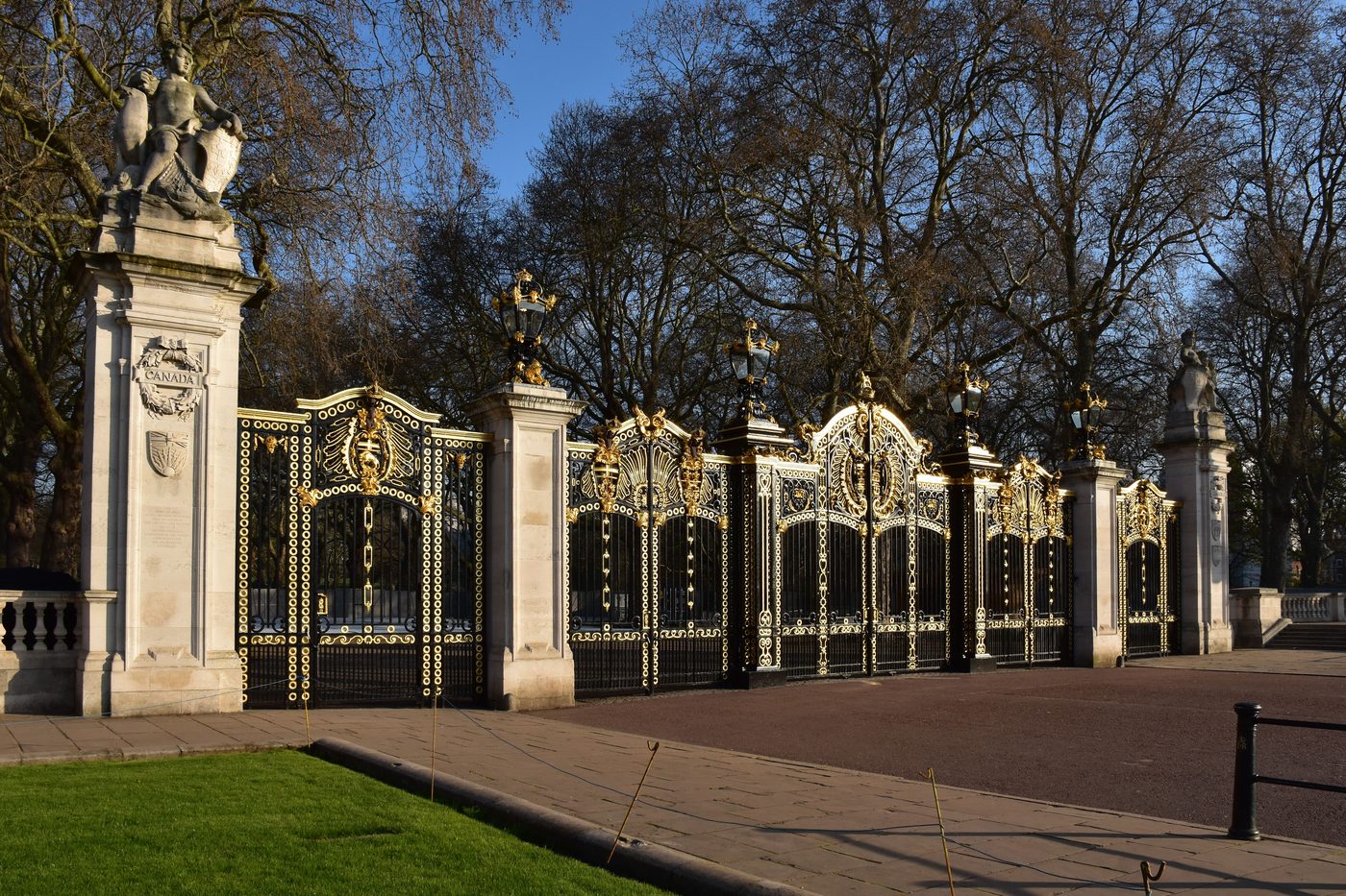 Row of black and gold ornamental iron gates between stone piers at a park entrance