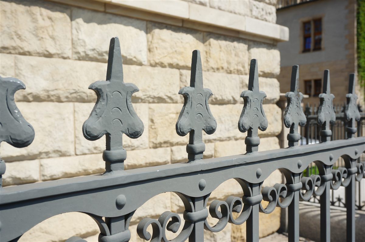 Grey painted wrought iron fence with fleur-de-lis finials in front of a limestone wall