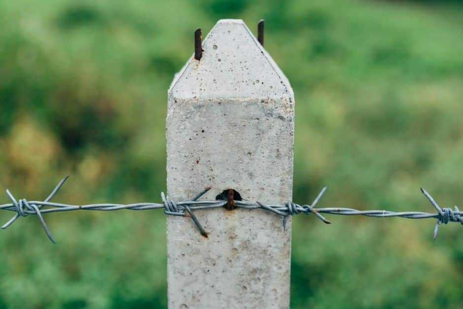 Content image 1 : Close-up of a fence post base set in a concrete footing with visible soil around it