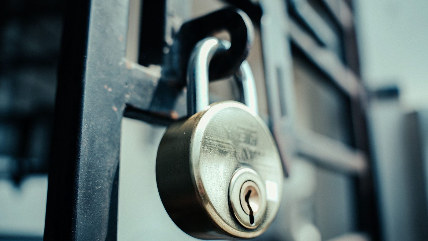 Close-up of a round steel padlock fastened through the latch of a dark metal bar gate
