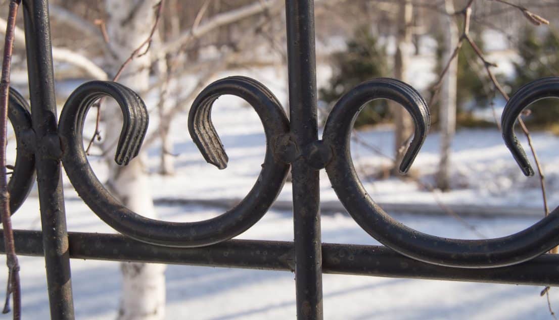 Close view of scrolled black wrought iron fence detail against a snowy garden