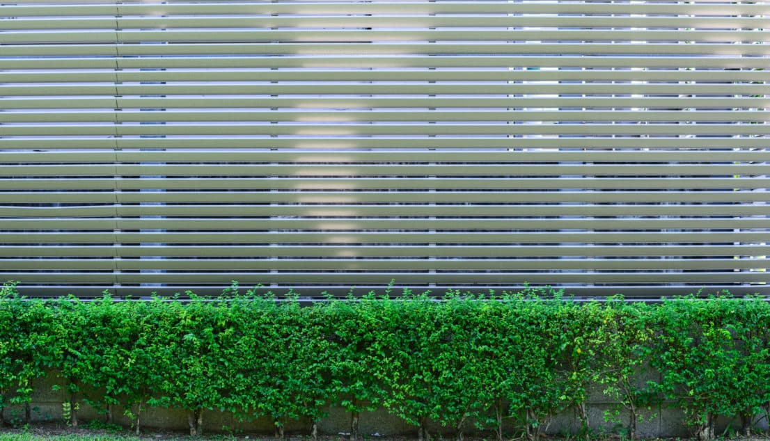 Horizontal metal slat fence running above a clipped green hedge