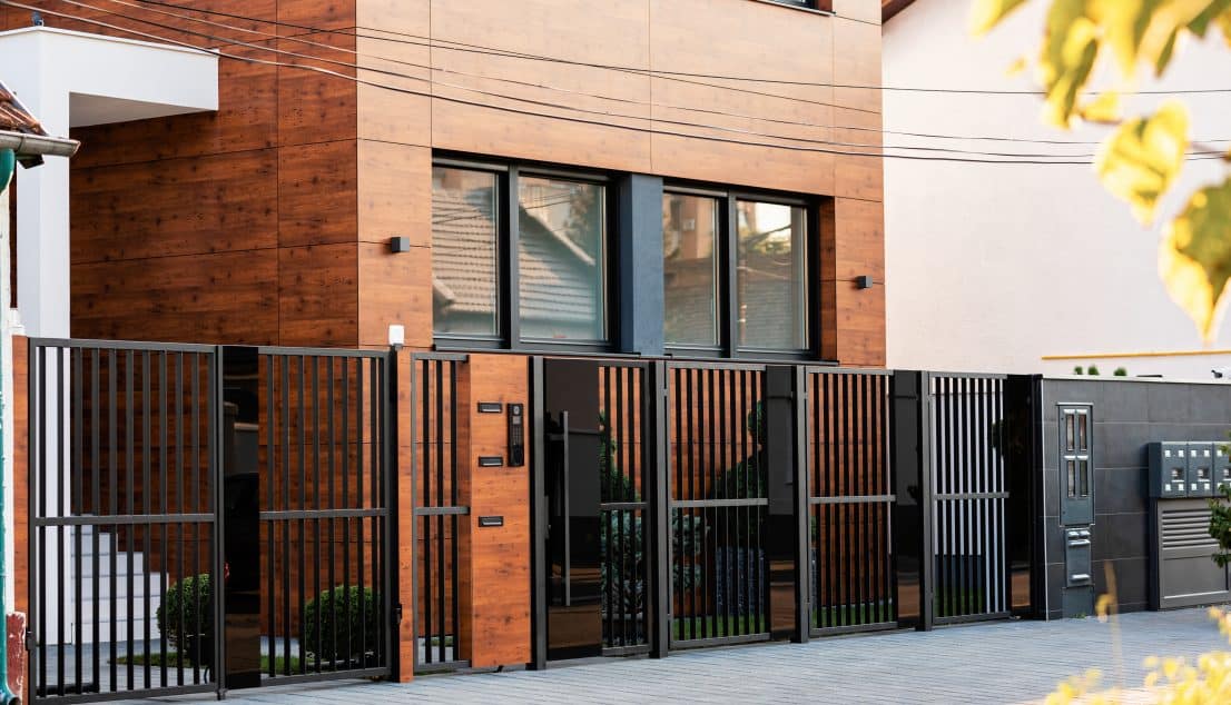 Black vertical bar fence and gates along the front of a modern brick and timber building