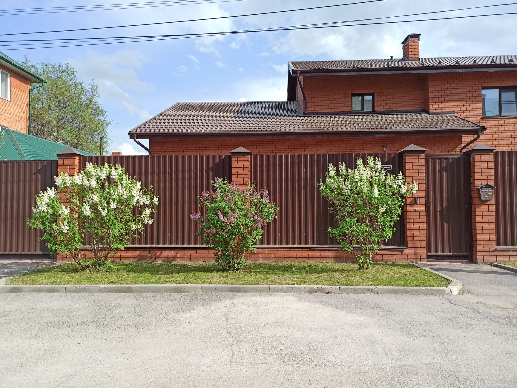 Elegant brick house with brown metal fence and flowering bushes in Berdsk, Russia