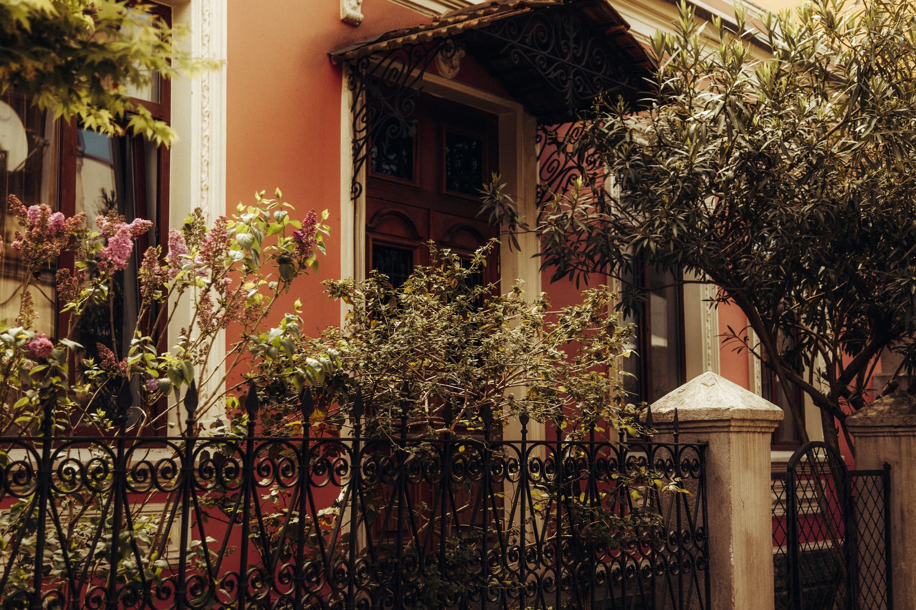 Beautiful garden with blooming flowers against an ornate facade and wrought iron fence.