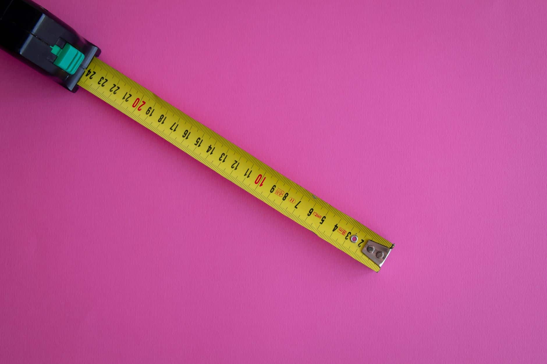 A yellow measuring tape extended on a vibrant pink background, offering ample copy space.