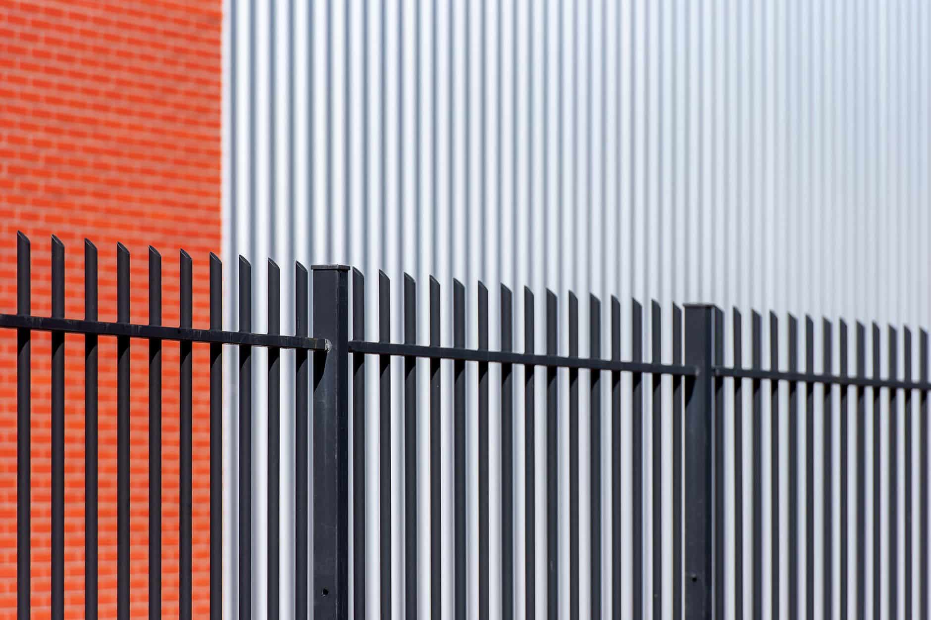 Black metal fence contrasts with red brick and corrugated metal backdrop, offering a sleek industrial look.
