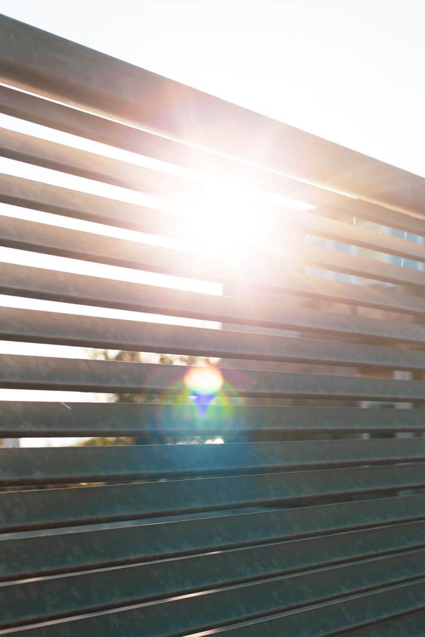 Bright sunlight filtering through metal slats creating lens flare and shadows.