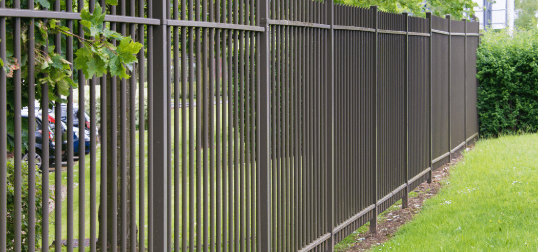 Tall dark metal picket fence running along a mown lawn beside a hedge